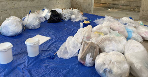 Pictured are tied bags of waste in white bags pictured over a blue tarp in preparation for the waste sort.